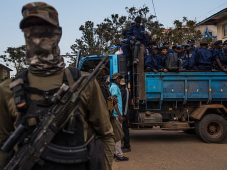 Armed African soldiers in camouflage fatigues surround a lorry full of police in blue uniforms 