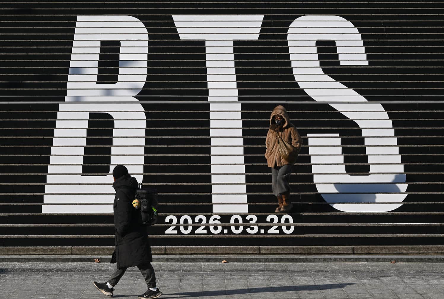 Pedestrians walk along the stairs displayed with the BTS logo